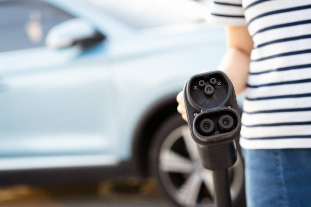 Unrecognizable Asian woman holding AC type 2 EV charging connector at EV charging station, woman preparing an EV - electric vehicle charging connector for recharge a vehicle.